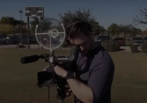 Man standing on a baseball field focusing a video camera