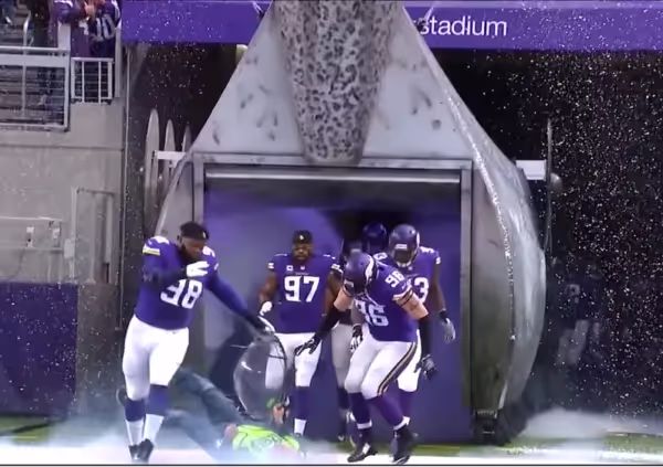 a group of football players running onto the field running over a parabolic microphones operator