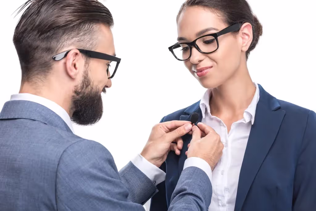 Man placing lapel mic on woman colleague.